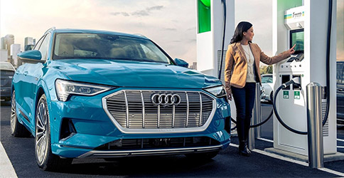 a woman recharging a blue Audi e-tron at a charging station