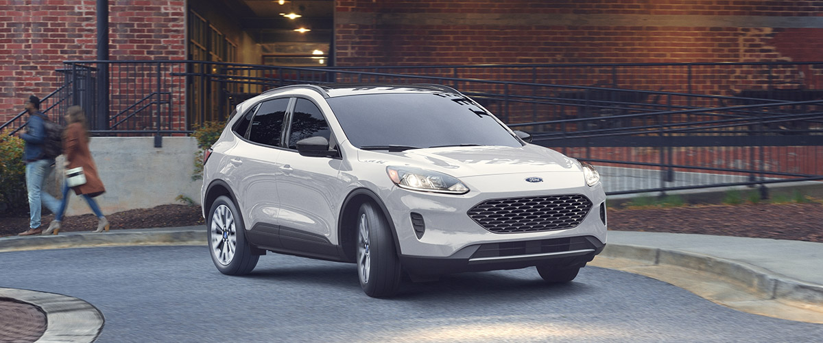 frontal view of white Ford Escape crossover parked in front of a red brick building 