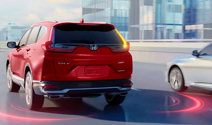 Rear driver-side view of the 2020 Honda CR-V in Radiant Red Metallic, driving on highway, with illustration showing Blind spot information system feature.