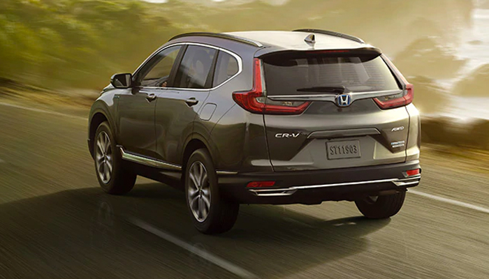 Rear driver-side view of the 2020 CR-V Hybrid Touring in Modern Steel Metallic, driving along a coastal highway.