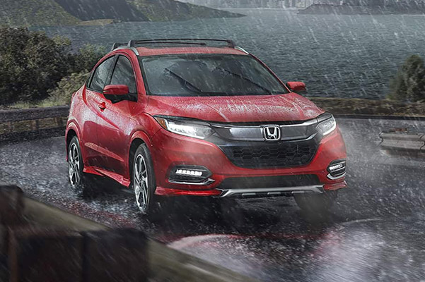 Milano Red 2020 Honda HR-V Touring shown driving around a curve in the road during a rain storm