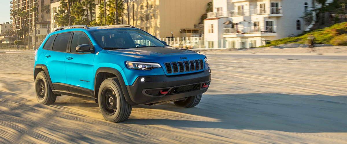 blue cherokee vehicle driving on sand in front of a beach