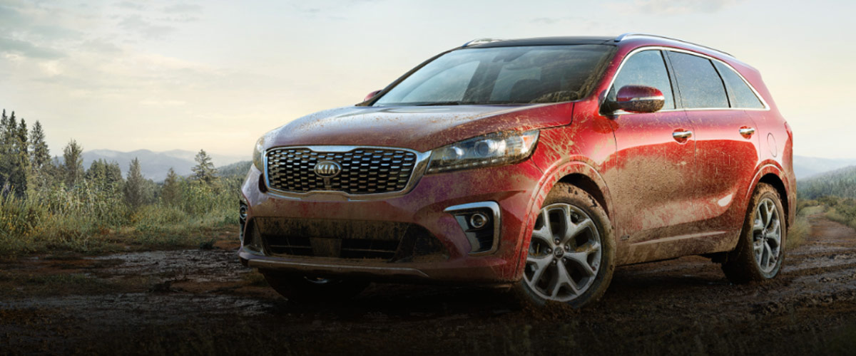 side view of Red Kia sorento suv with mud all over the place parked on a dirt road