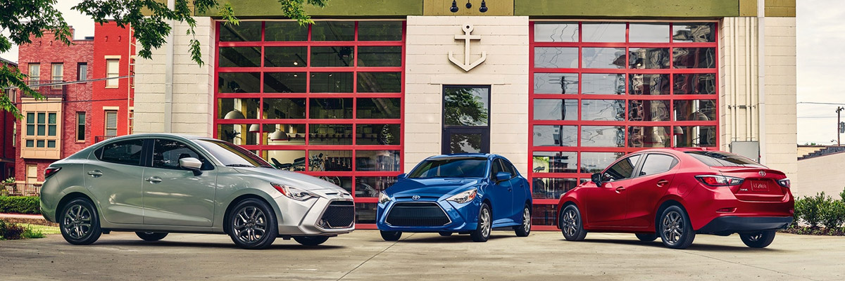 Image of a white 2020 Toyota Yaris, a blue 2020 Toyota Yaris and red 2020 Toyota Yaris parked facing eachother in front of a building