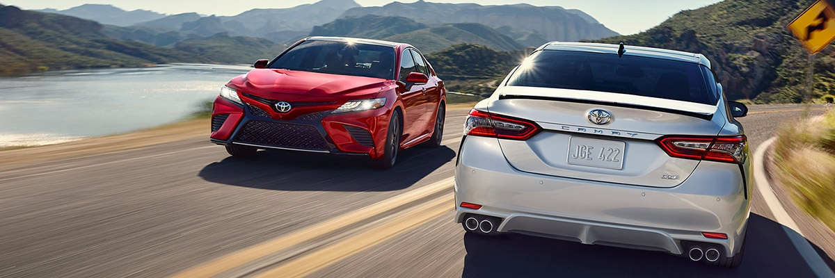 A red 2020 Toyota Camry driving past a white 2020 Toyota Camry going the opposite direction