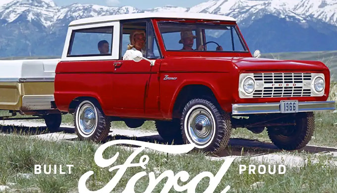 A family riding in a 1966 Ford Bronco Sport Wagon in Royal Maroon with Wimbledon White roof pulling a pop up camper trailer on a two track trail in the mountains