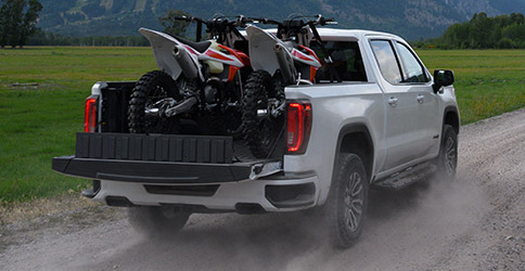 2021 GMC Sierra 1500 driving down a dirt road with dirt bikes in the trailer