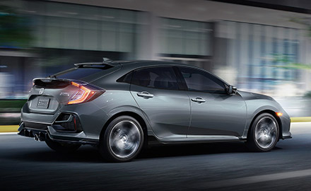 side view of honda civic hatchback on the road with headlights on