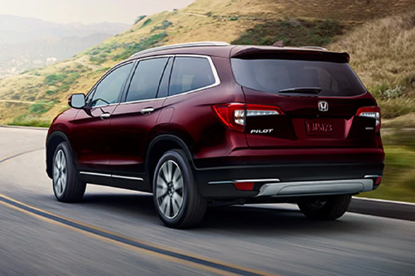 Rear view of a 2021 Honda Pilot shown in Deep Scarlet Pearl driving down a highway