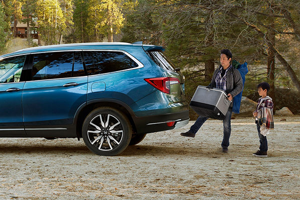 Side view of a 2021 Honda Pilot shown in Steel Saphire Metallic with a father and son packing it for a camping trip