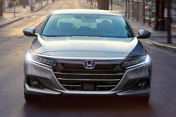 Front view of the 2021 Honda Accord Hybrid, shown in Lunar Silver Metallic, driving down an open road.