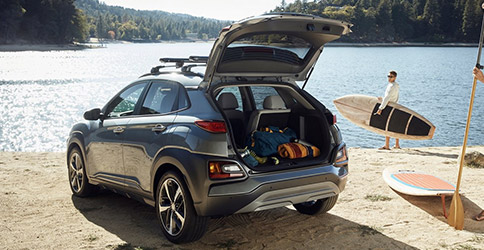 rear profile of hyundai kona suv with trunk door open parked on the edge of a lake