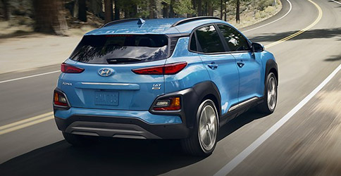 rear side profile of hyundai kona suv in blue color driving on a road surrounded by trees