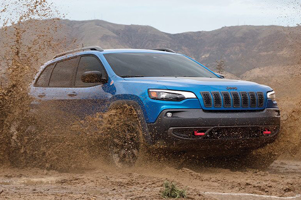 A 2021 Jeep Cherokee churns up mud from its wheels as it's driven off-road.