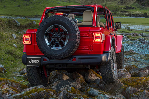 A rear view of the 2021 Jeep Wrangler Rubicon as it is driven on a rocky trail near a stream.