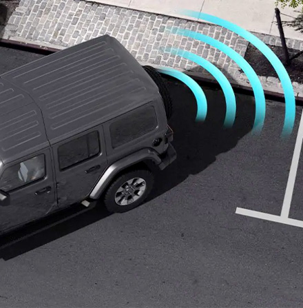 Illustration of sensors monitoring the area behind the 2021 Jeep Wrangler Sahara as it parallel parks at a curb.