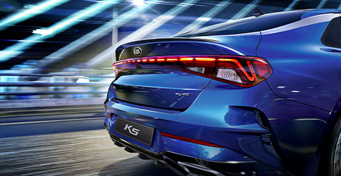 rear tail light view of the 2022 blue kia k5 zooming down the road