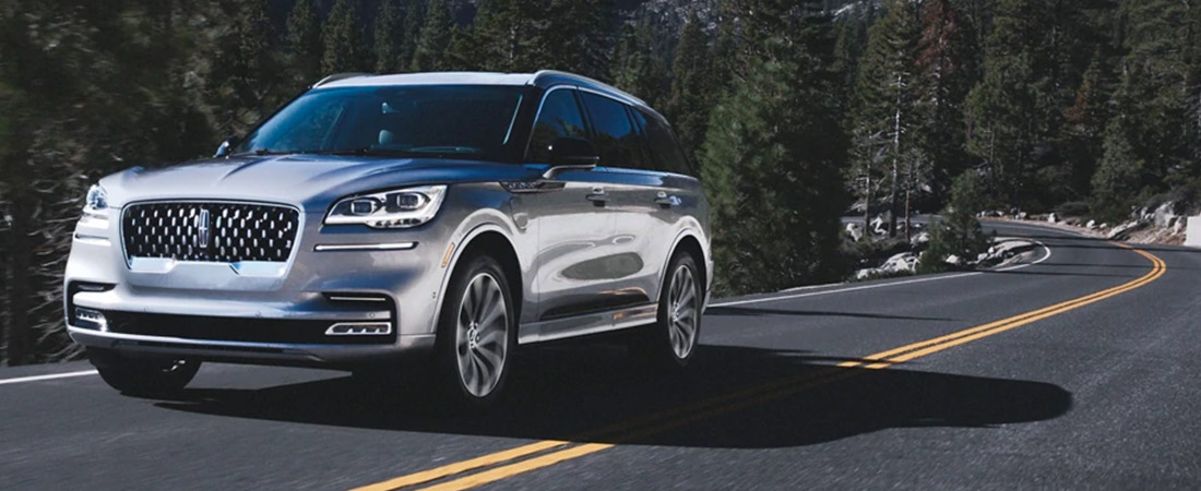 A 2021 Lincoln Aviator Grand Touring model is shown being driven on a tree lined road