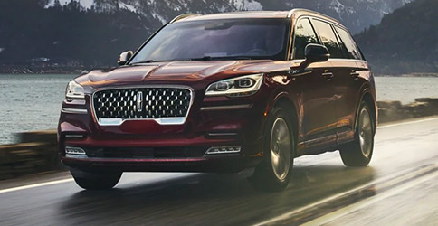 A 2021 Lincoln Aviator is shown being driven along a road in a breathtaking river valley
