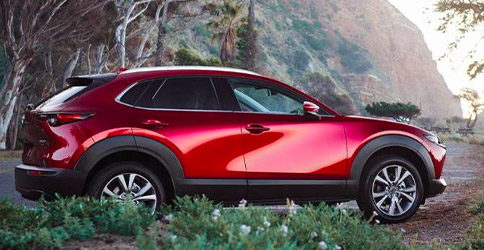 side profile of Mazda CX-30 suv in red color parked on a side of a road surrounded by trees
