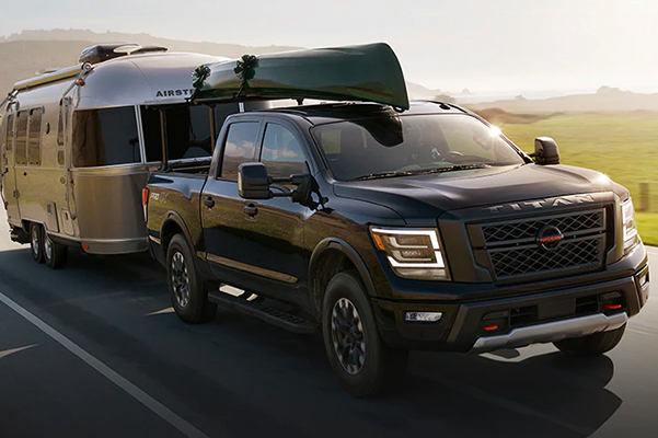 2021 Nissan TITAN on highway with canoe on top and towing an airstream through green hills