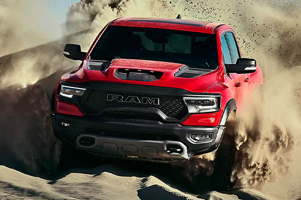 Display The 2021 Ram 1500 TRX being driven over a sand dune, churning up a large dust cloud.