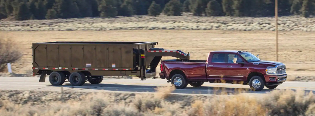 ram 3500 driving down a road towing a dumpster
