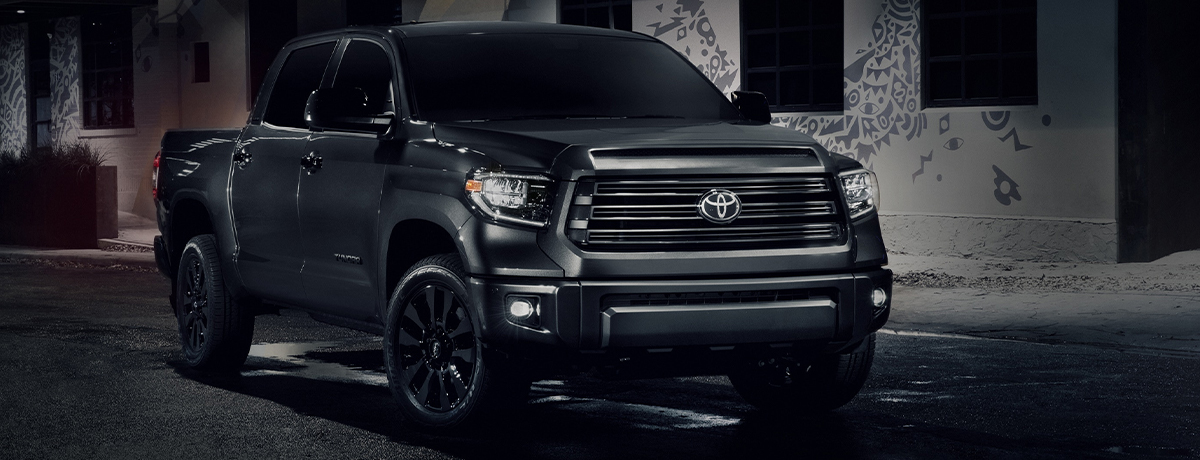 side and frontal view of a black Toyota Tundra truck at night with the headlighst on