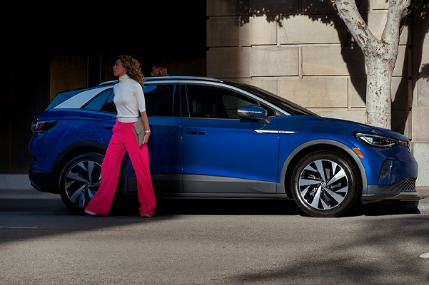 A woman walks away from the passenger side of an ID.4 in Dusk Blue Metallic, parked on an urban street.