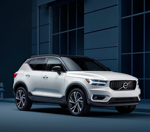 A Volvo XC40 stands parked along a blue facade