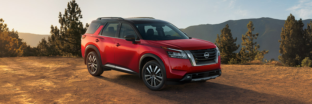 side profile of 2022 Nissan Pathfinder in red color parked on tough terrain with mountains in the background