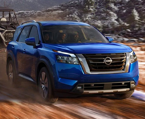 side profile of 2022 nissan pathfinder in blue color towing recreational vehicles on a dirt road with snow.