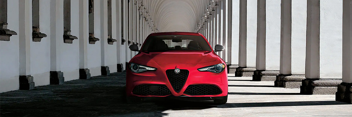 A head-on view of a red 2022 Alfa Romeo Giulia Veloce parked beside large columns in the alcove of an ornate building.