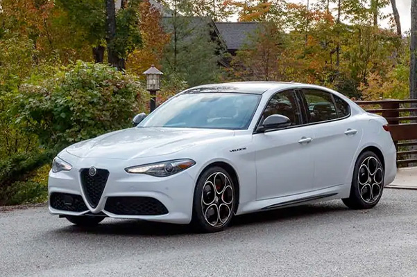 A white 2022 Alfa Romeo Giulia Veloce parked next to a cabin in the woods.