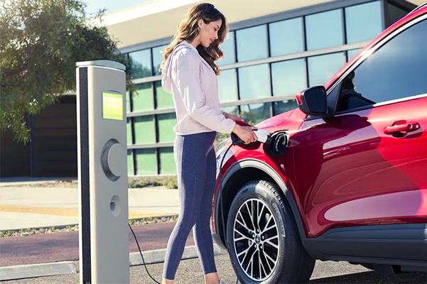 Woman at a public station charging a 2021 Ford Escape plug in hybrid in Rapid Red Metallic Tinted Clearcoat extra cost color