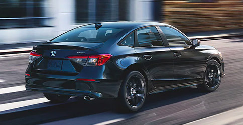 Rear passenger-side view of the 2022 Honda Civic Sport Sedan in Crystal Black Pearl, making a right turn on a city street.
