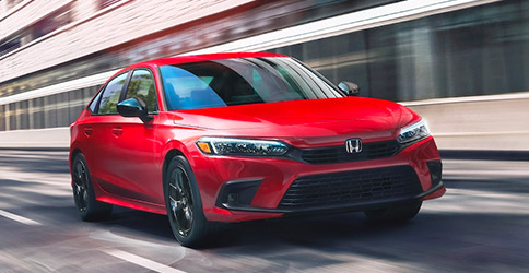 Front driver-side view of the 2022 Honda Civic Sport Sedan in Rallye Red, driving on a city street.