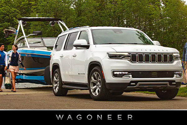 Display The 2022 WAGONEER towing a motorboat on a country road.