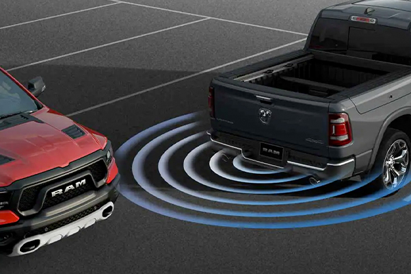 The 2022 Ram 1500 in a parking spot with sensor bars coming from the rear of the vehicle detecting another truck passing behind it.