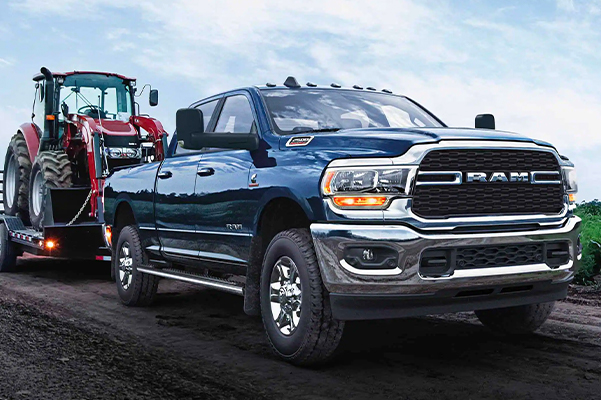 The 2022 Ram 2500 towing a flatbed with a tractor on it.