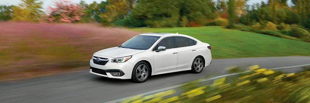 2022 Subaru Legacy Touring XT shown in Crystal White Pearl. Driving at high speed with rural background