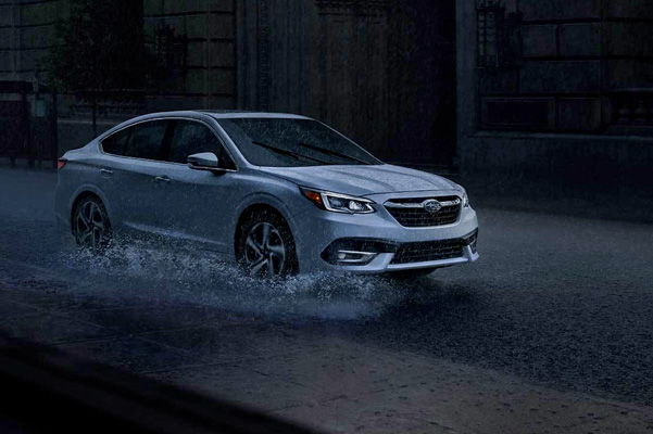 2022 Subaru Legacy Touring XT shown in Crystal White Pearl. Driving at in the rain with a city background