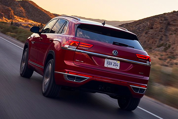 Atlas Cross Sport in Aurora Red Metallic driving on two-lane mountain road, as seen from the rear driver’s side.