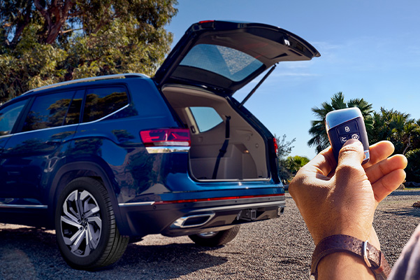 Rear, driver’s side shot of the Atlas in Tourmaline Blue Metallic. Hand in foreground holds a key fob remote as the power liftgate raises.