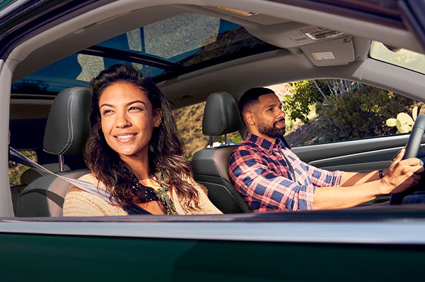 A man and woman cruise in their Racing Green Metallic Atlas with the windows down.