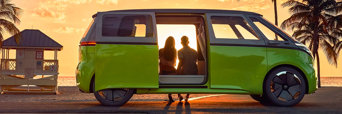 Two people watch the sunset while sitting inside an open ID. Buzz concept vehicle parked near the ocean.