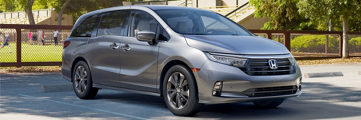 Front passenger-side view of the 2023 Honda Odyssey Elite in Lunar Silver Metallic parked next to a soccer field. 
