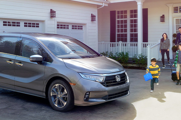 Front passenger-side view of the 2023 Honda Odyssey Elite in Modern Steel Metallic parked in front of a house. 
