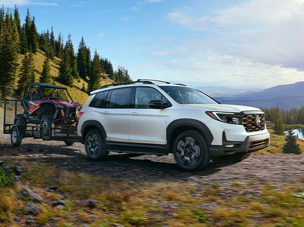 2023 Honda Passport parked in front of a lake towing a tractor