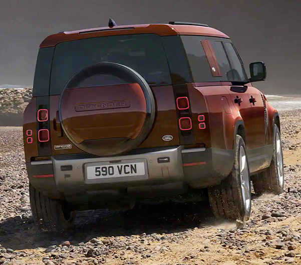 Rear view of a red 2023 Land Rover Defender 130 driving over a gravel terrain
